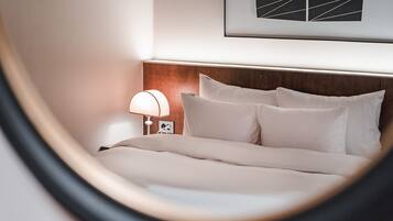 A neatly made bed with white linens, a wooden headboard, and a bedside lamp.