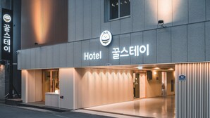 Fachada de hotel con diseño moderno, que presenta un cartel con texto en inglés y coreano, y una iluminación destacada.