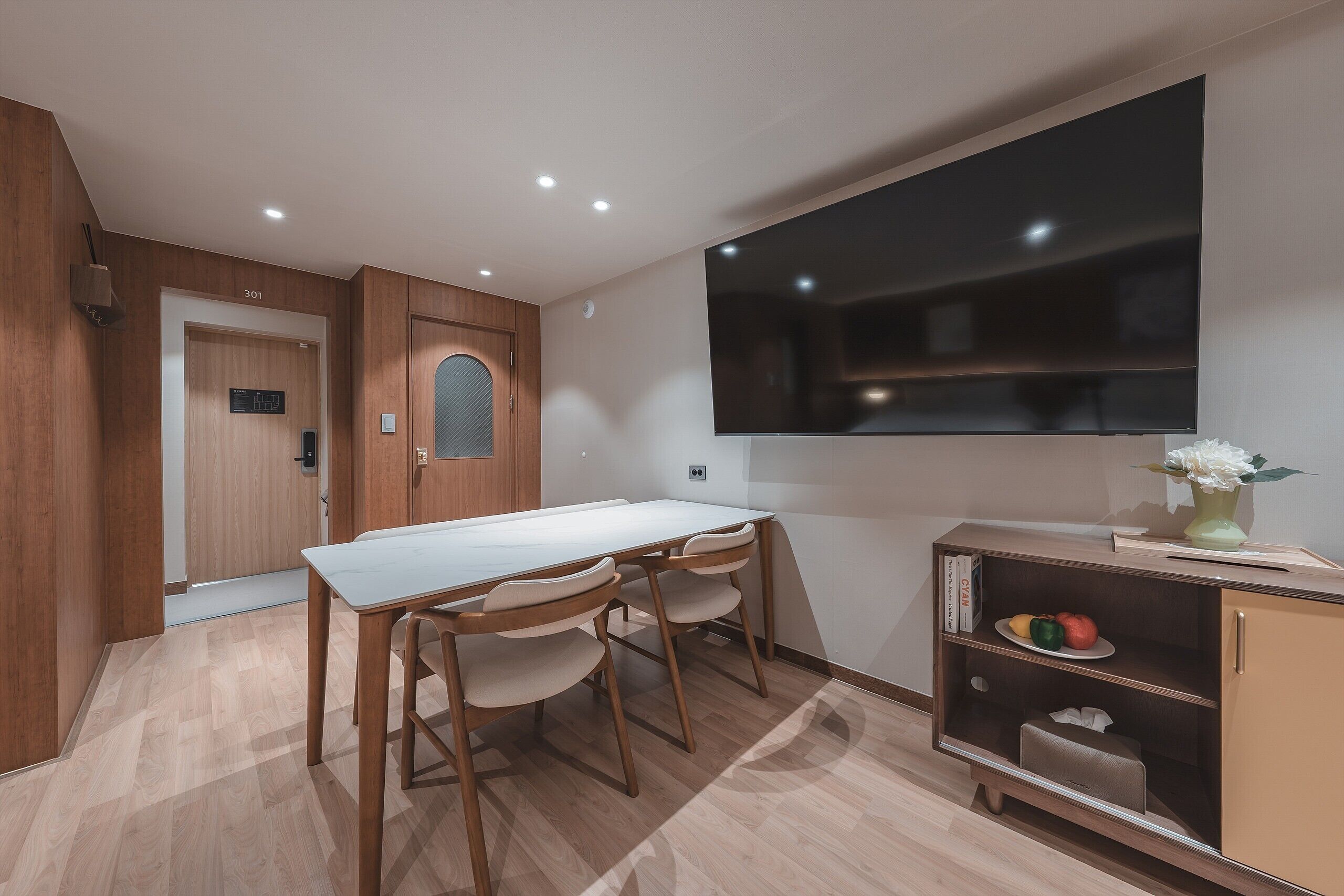 A modern kitchen with a dining table, chairs, a built-in TV, and a small cabinet with a vase.