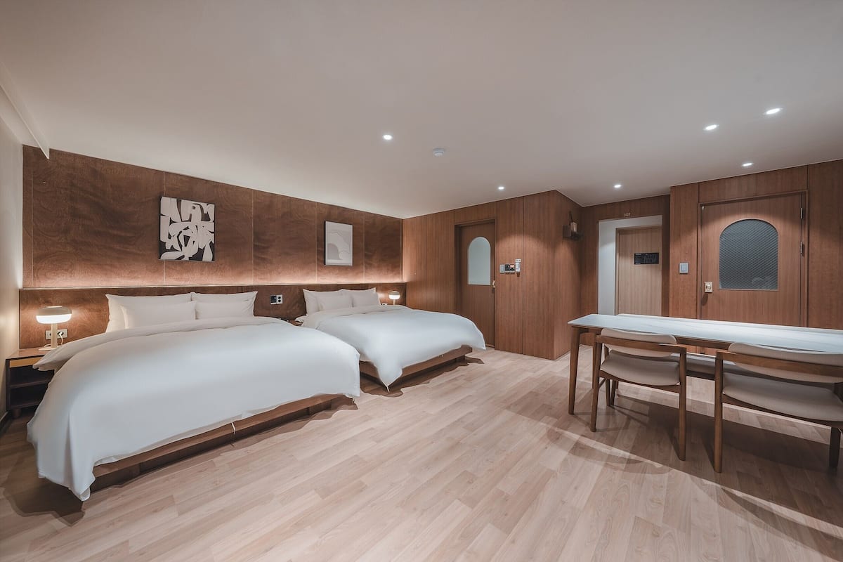 Hotellihuone, jossa on kaksi sänkyä, puulattia, pöytä ja peilillä varustettu ovi.