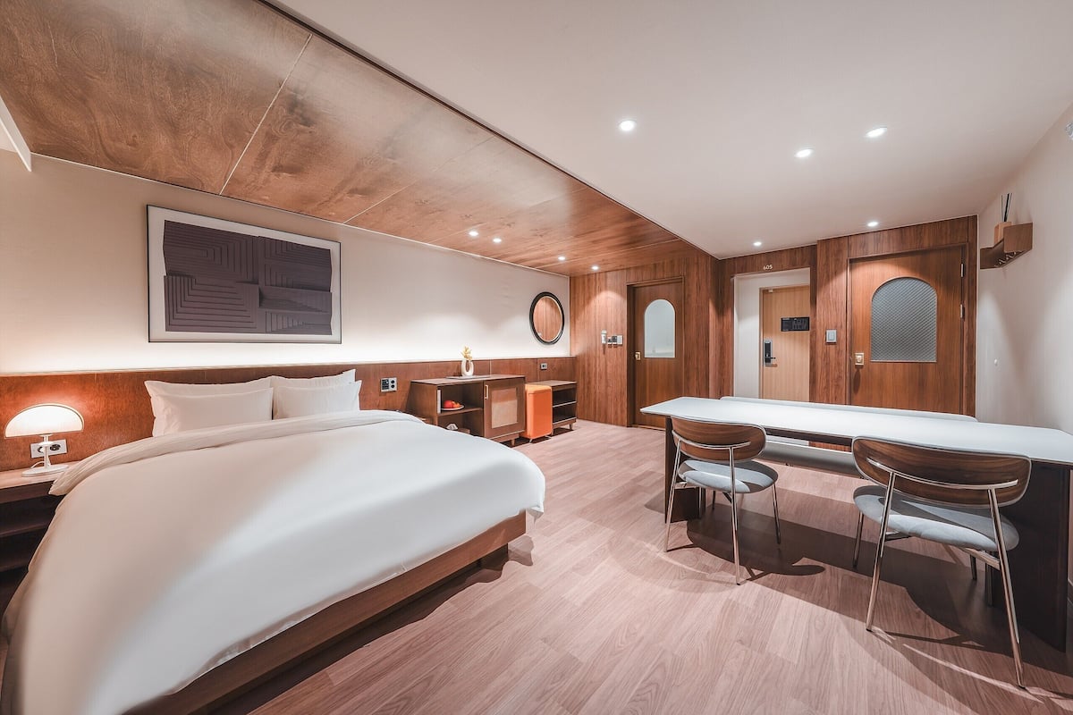 Moderni hotellihuone, jossa on suuri sänky, työpöytä kahdella tuolilla, pieni pöytä ja peili.