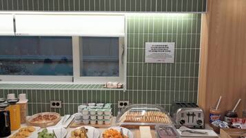A breakfast buffet with various food items, a toaster, and a sign on the wall.