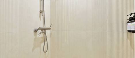 A shower with a handheld showerhead and a wall-mounted faucet.