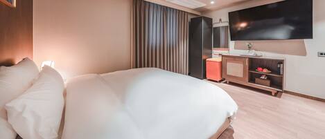 A modern hotel room with a large bed, a flat-screen TV mounted on the wall, a wooden nightstand, and a large window with curtains.