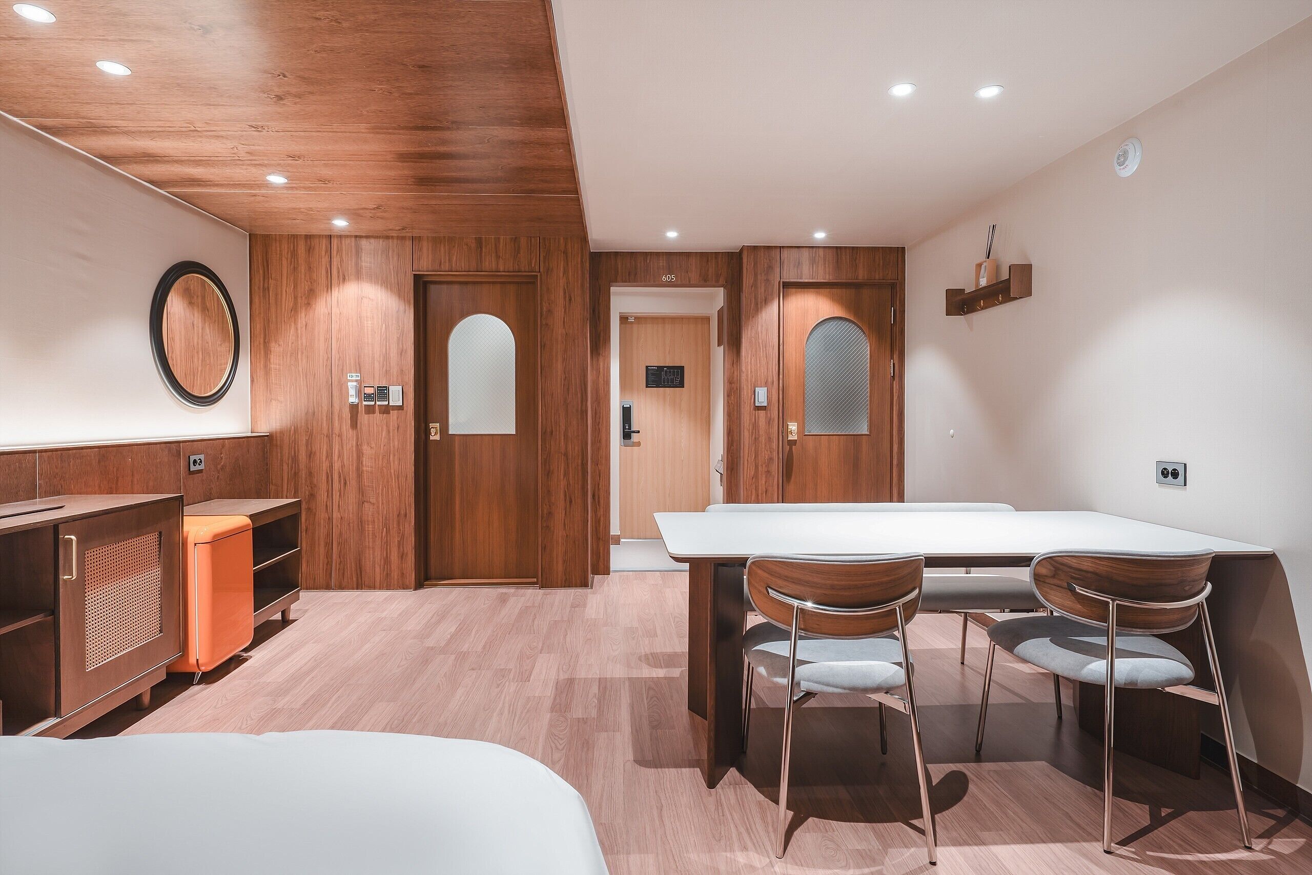 Habitación de hotel moderna con techo de madera, cama blanca, escritorio de madera y zona de comedor con mesa y sillas.