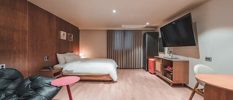 A modern hotel room with a bed, a leather sofa, a small round table, a desk, a TV, and a wardrobe.
