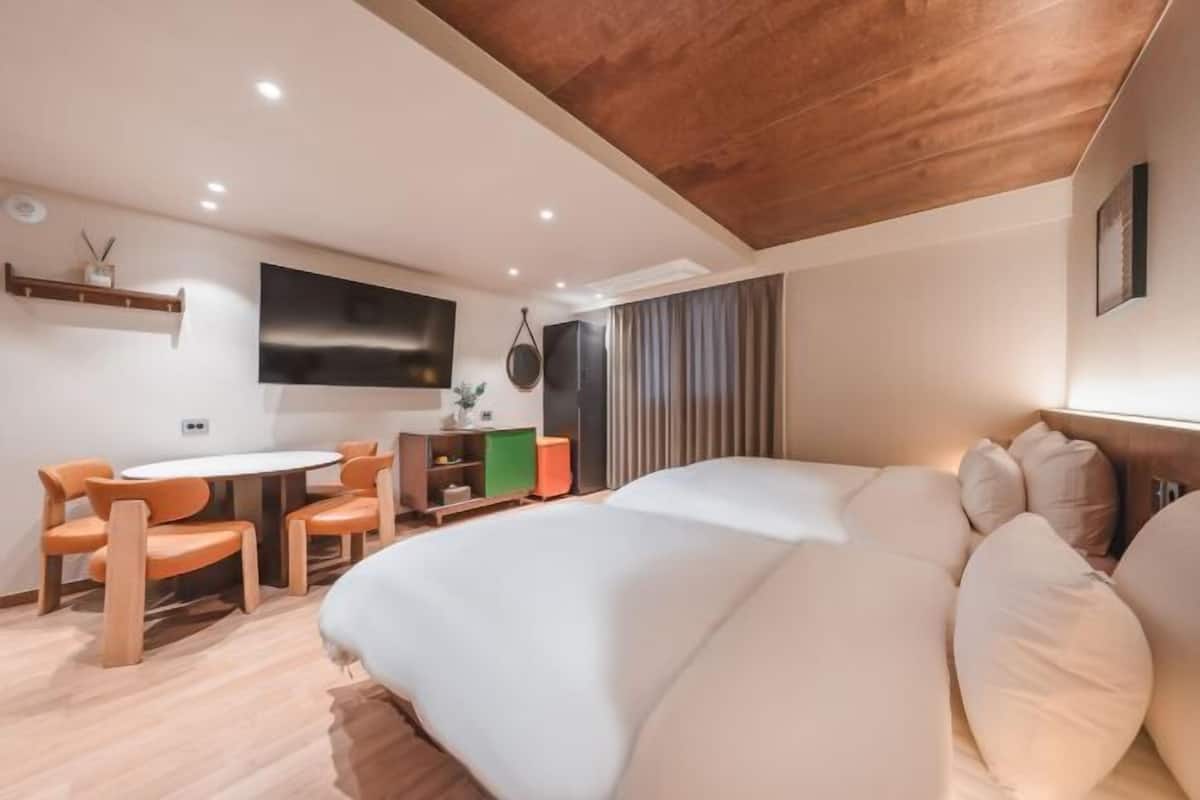 Moderni hotellihuone, jossa on puinen katto, suuri sänky, työpöytä tuolilla ja seinälle asennettu televisio.