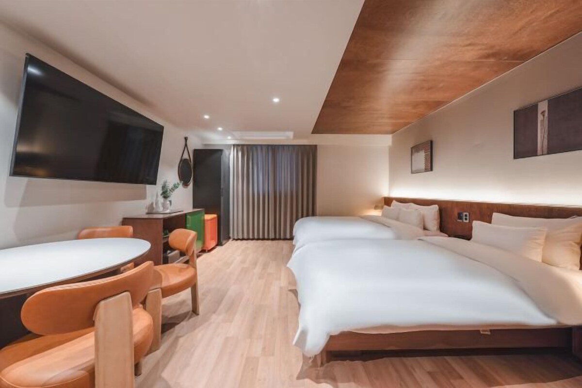 Una habitación de hotel moderna con una cama grande, un escritorio con sillas, un televisor de pantalla plana y un techo de madera.