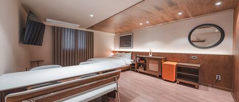 A modern hotel room with a wooden ceiling, a bed, a desk, a chair, and a small orange ottoman.