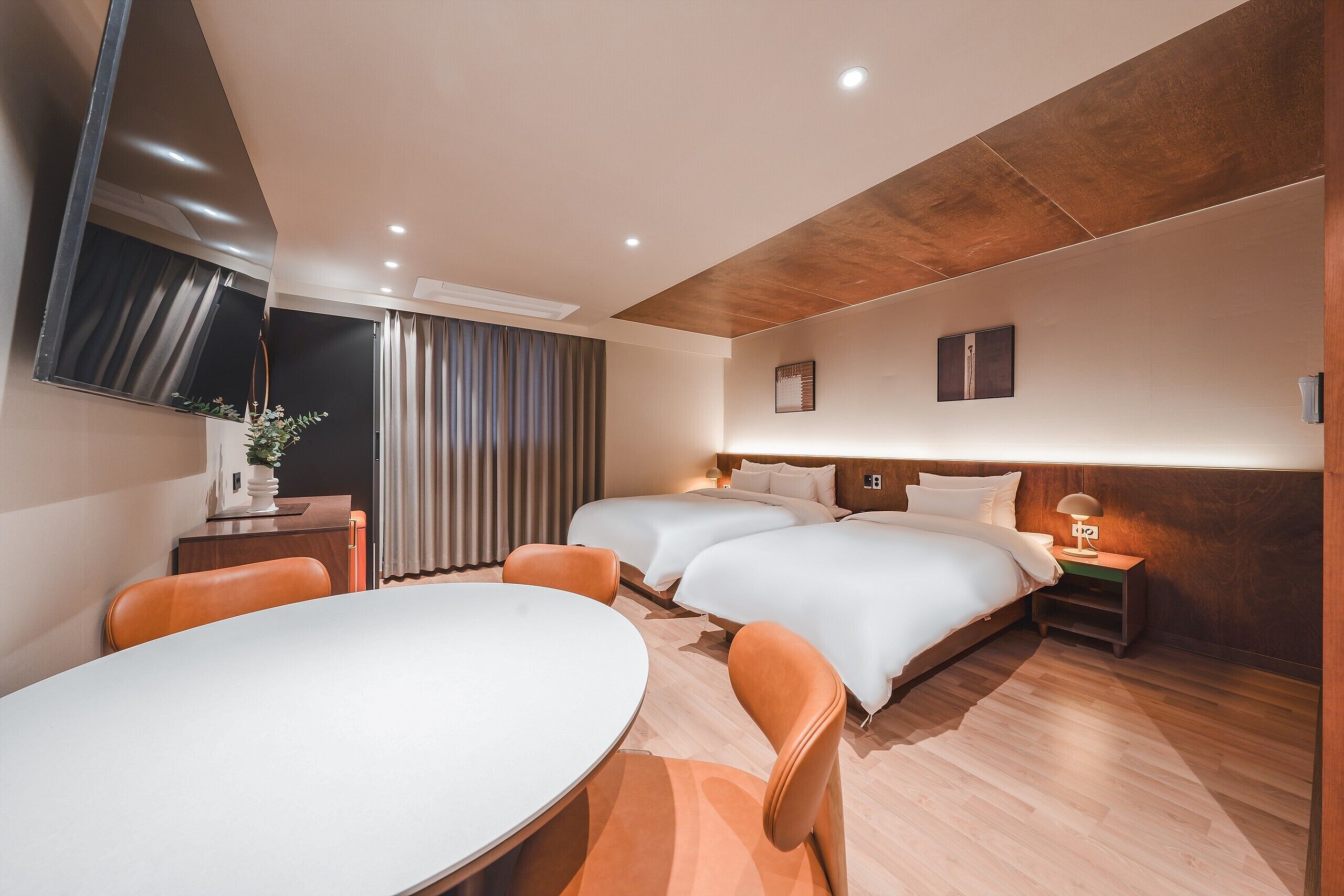 A modern hotel room with a large bed, a desk with a chair, a TV mounted on the wall, and a window with curtains.