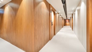 Un pasillo moderno de hotel con paneles de madera en las paredes, una alfombra blanca y varias puertas que dan a las habitaciones.