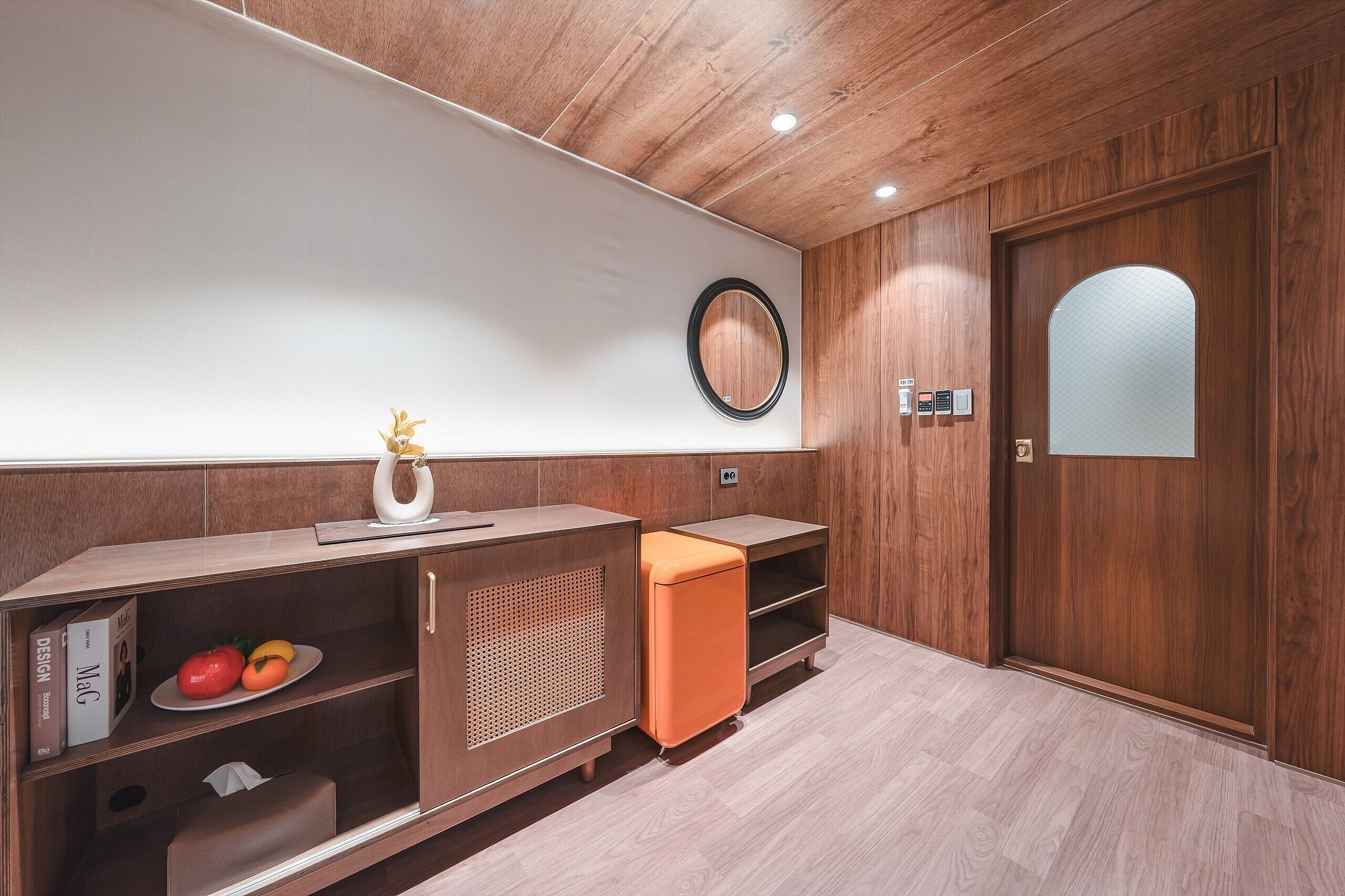 A modern room with wooden paneling, a round mirror, and a door with a frosted glass panel.