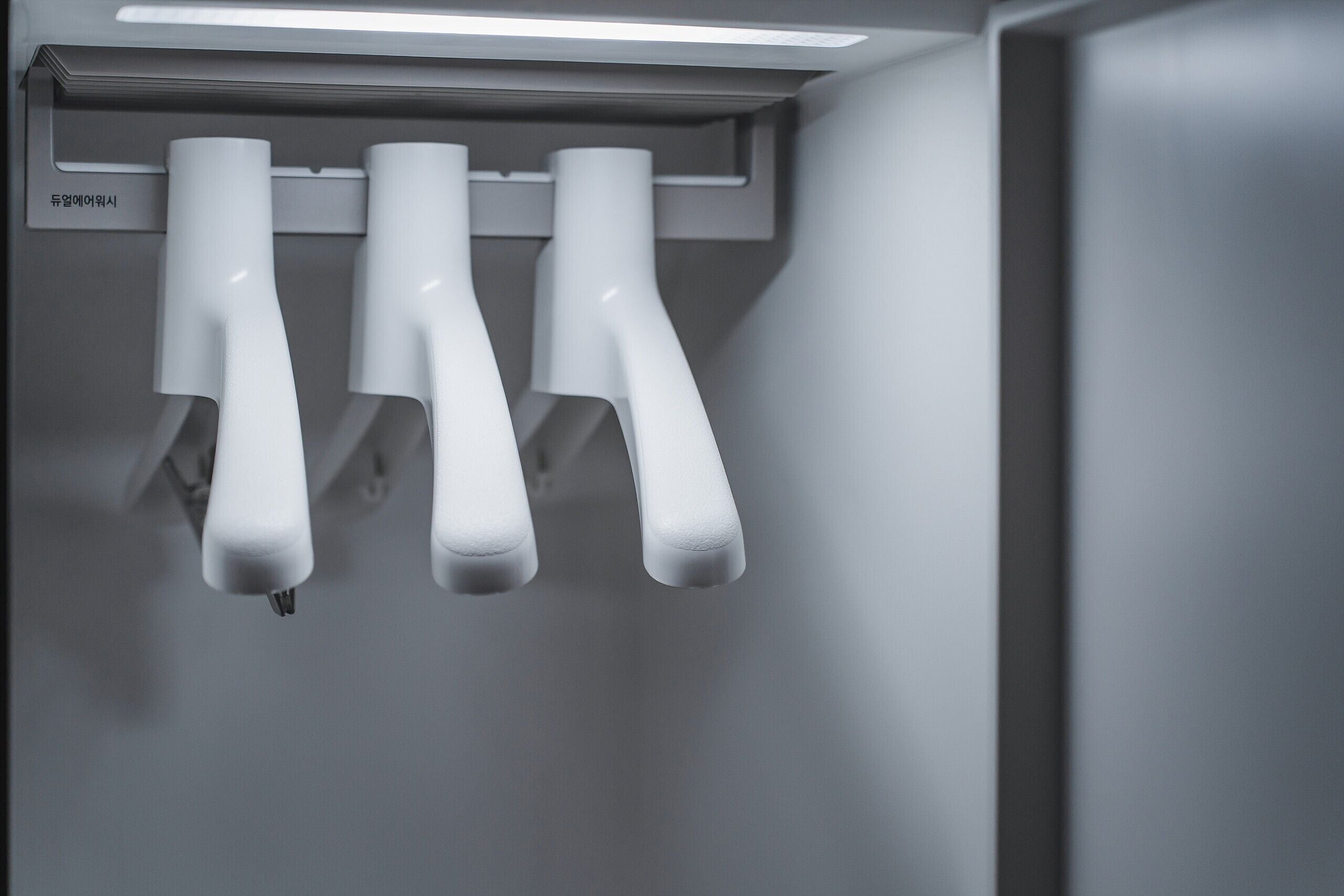 Um banheiro moderno e minimalista, com três chuveiros brancos e curvos fixados na parede.