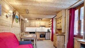 A cozy cabin-style room with a wooden interior, a dining table with chairs, a red sofa, and a small wooden table.