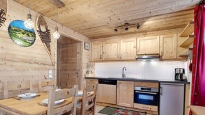 A wooden interior with a dining table, chairs, a kitchen area with cabinets, a sink, and a refrigerator.