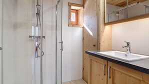 A modern bathroom with a glass-enclosed shower, wooden cabinetry, and a large mirror above the sink.
