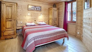 A wooden cabin bedroom with a bed, two nightstands, a wardrobe, and a window with a view.