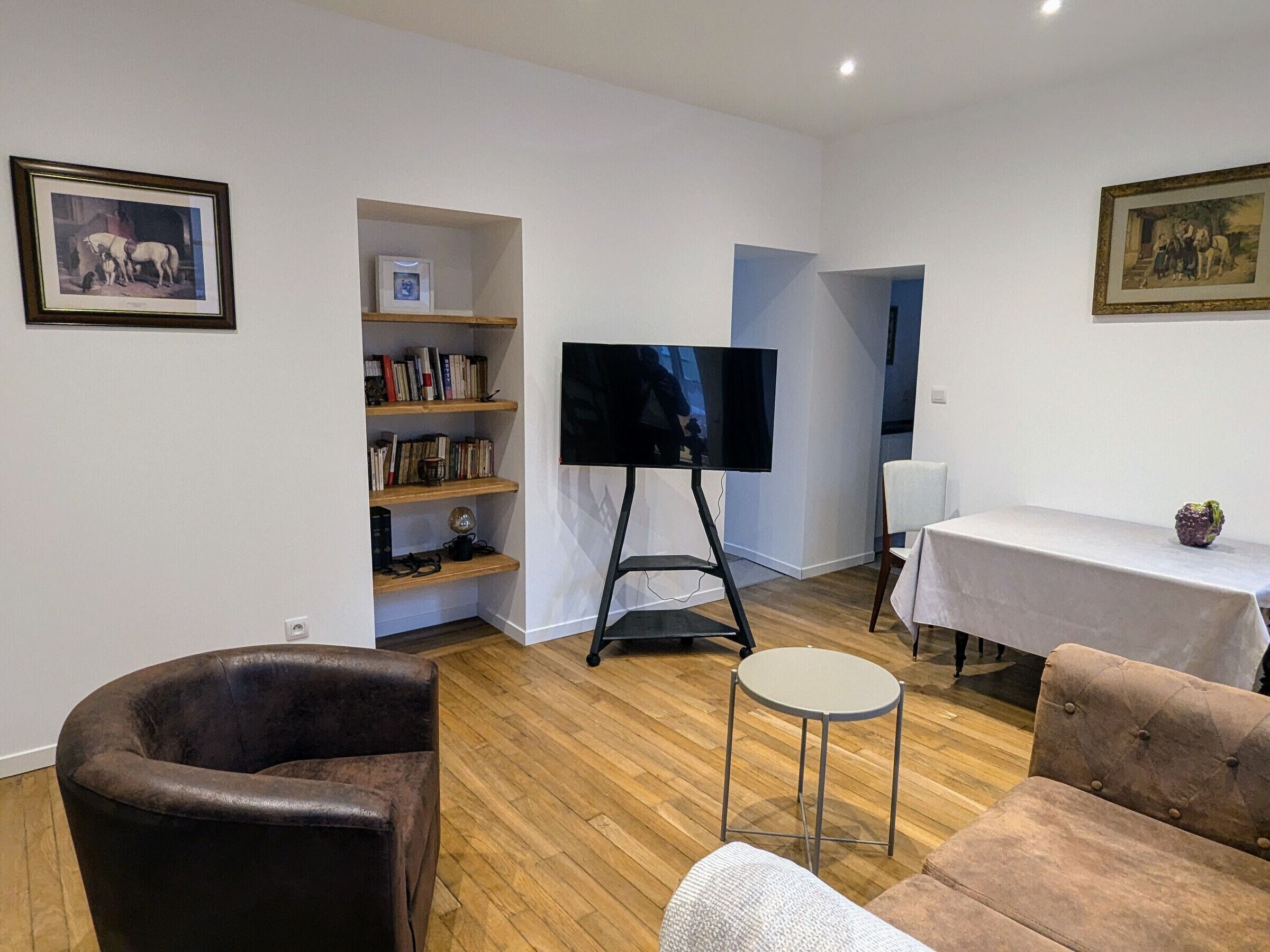 Una sala de estar con un sillón de cuero, un sofá, un televisor sobre un mueble bajo, una estantería y una mesita redonda.