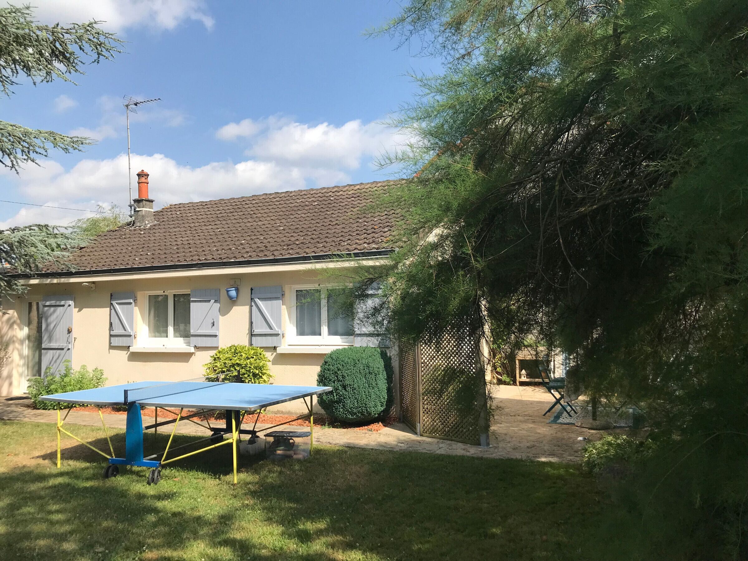 A house with a tiled roof, a chimney, and a solar-powered table in the yard.