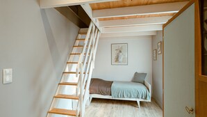 Una camera da letto compatta con una scala in legno, un letto con coperta grigia e un'opera d'arte astratta incorniciata appesa al muro.