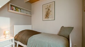 Una camera da letto con un letto, un comodino con una lampada, una mensola con dei libri e un quadro appeso alla parete.