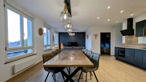 Une cuisine moderne dotée d’un îlot central, un coin repas avec une grande table et des chaises, et un espace de vie avec un canapé et une télévision.