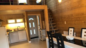 A compact kitchen with a sink, stove, and cabinets, a dining area with a table and chairs, and a wooden interior. - Charming lodge in Vosges forest with private parking (Granges-Aumontzey-Aumontzey)