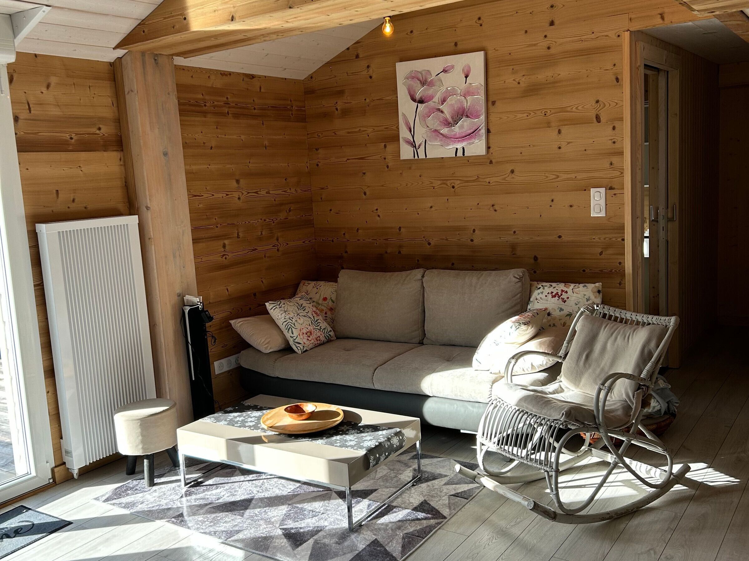 A cozy log cabin interior with a sofa, rocking chair, and a painting of flowers on the wall.