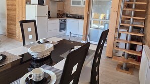 A modern kitchen with wooden cabinets, a microwave, and a stove. There is a dining area with a table and chairs, and a staircase leading to an upper level. - Charming lodge in Vosges forest with private parking (Granges-Aumontzey-Aumontzey)