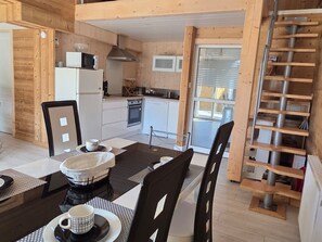 A modern kitchen with wooden cabinets, a microwave, and a stove. There is a dining area with a table and chairs, and a staircase leading to an upper level.