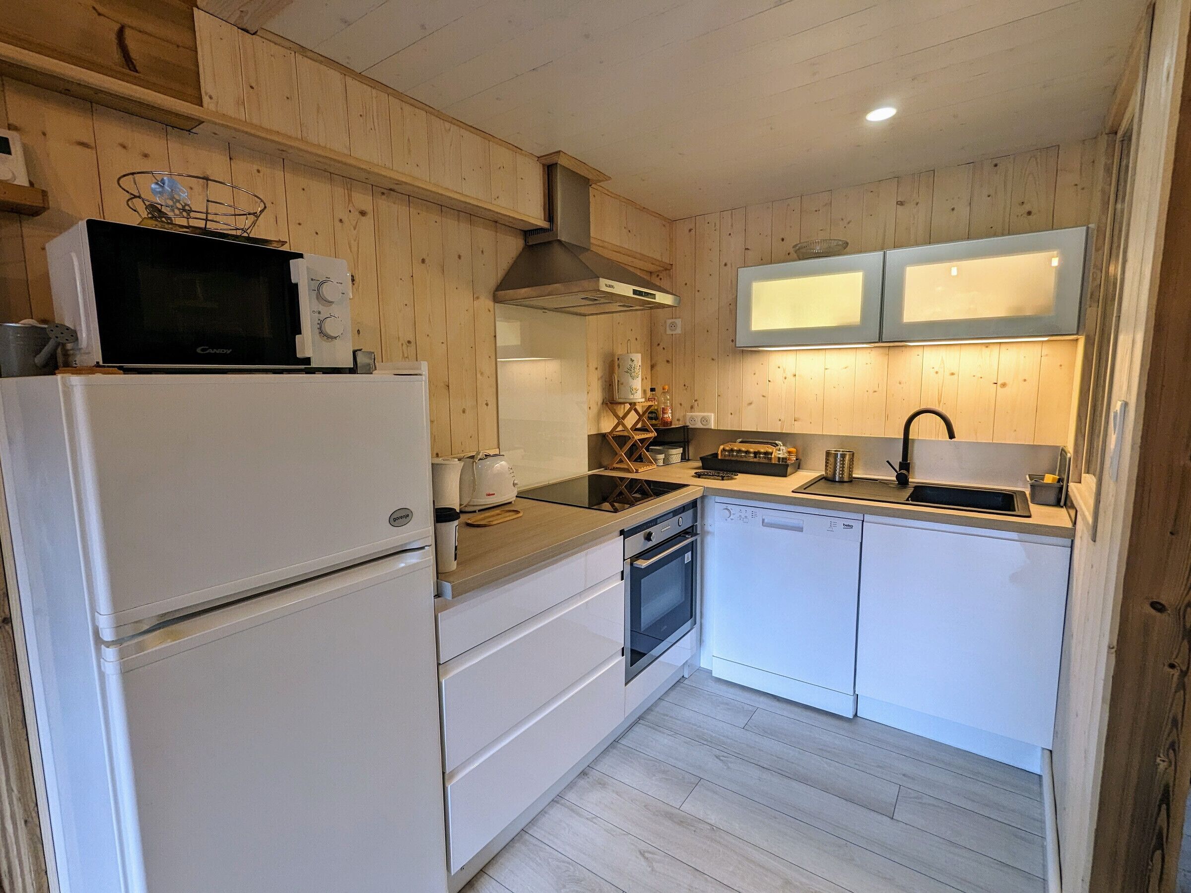 Une cuisine compacte avec des panneaux de bois, un four à micro-ondes, une cuisinière, un évier et un lave-vaisselle.