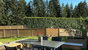 An outdoor patio with a glass-top table and chairs, surrounded by wooden deck and a wooden fence. - Charming lodge in Vosges forest with private parking (Granges-Aumontzey-Aumontzey)