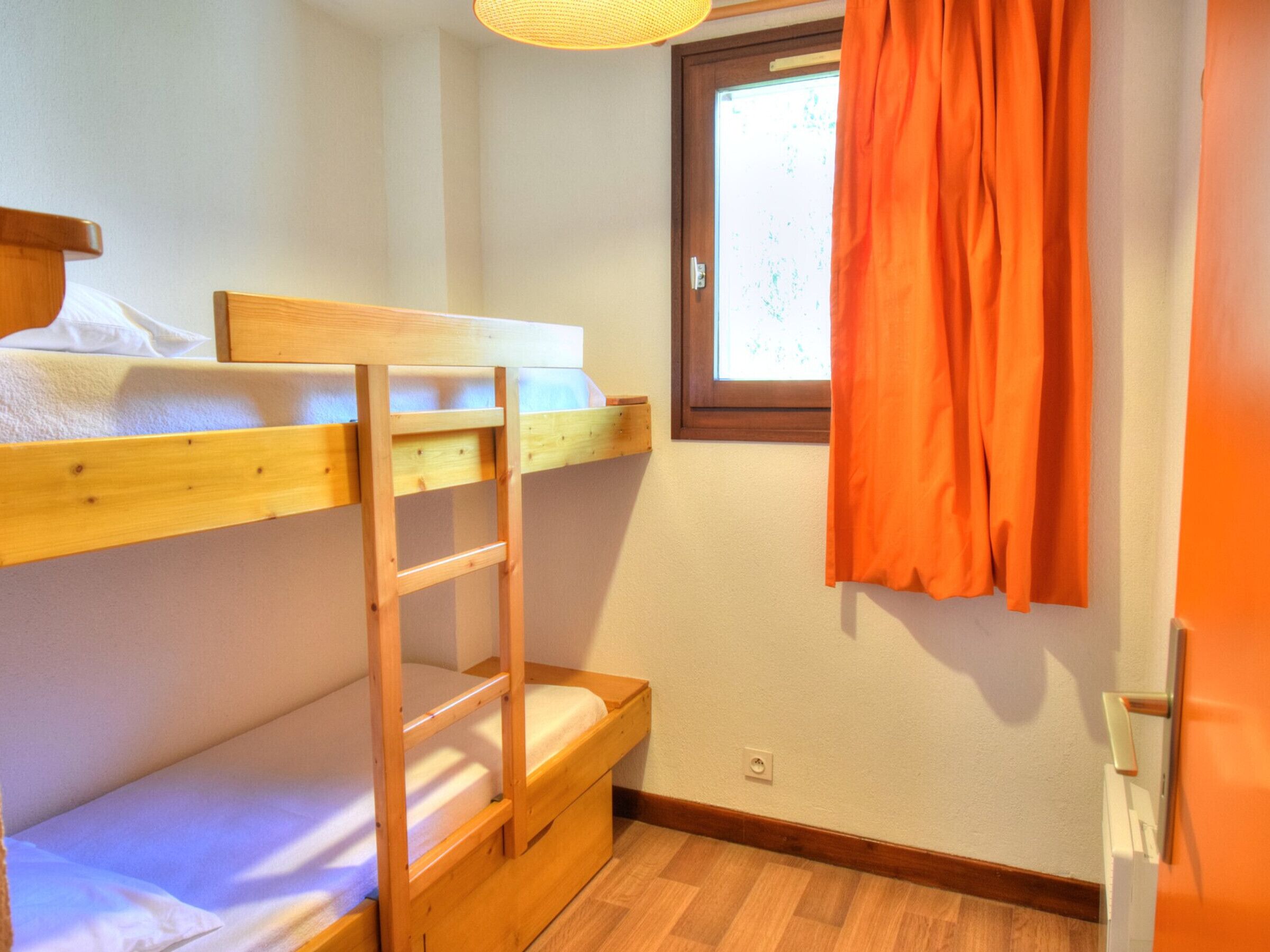 Ein Schlafzimmer mit Etagenbetten, einer Holzleiter, einem Fenster mit Vorhängen und einer Tür.