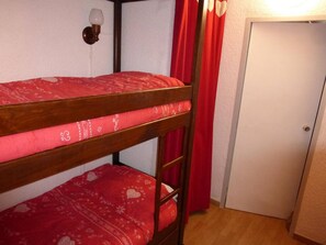 Cozy room with a bunk bed and a red patterned mattress, featuring a white door, a red curtain, and a wall-mounted light fixture.
