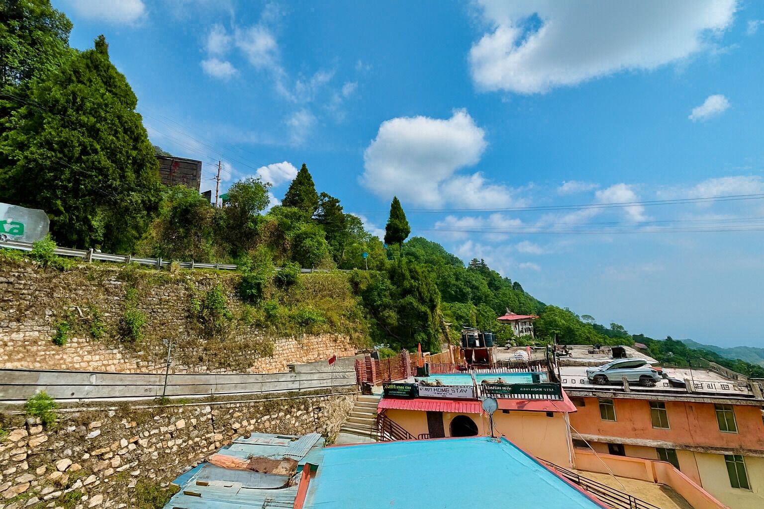 Paesaggio montuoso con cielo sereno, un muro di pietra e edifici con tetto rosso.