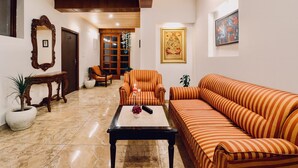 Un salón con un sofá a rayas, un sillón y una mesa de centro. Hay un espejo, una puerta y un cuadro en la pared.