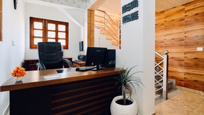 Mostrador de recepción con una computadora, una planta en maceta y una escalera de madera que lleva a un nivel superior.