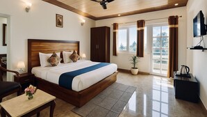 Una habitación de hotel con una cama grande, un ventilador de techo, un televisor, un escritorio y una planta en maceta.