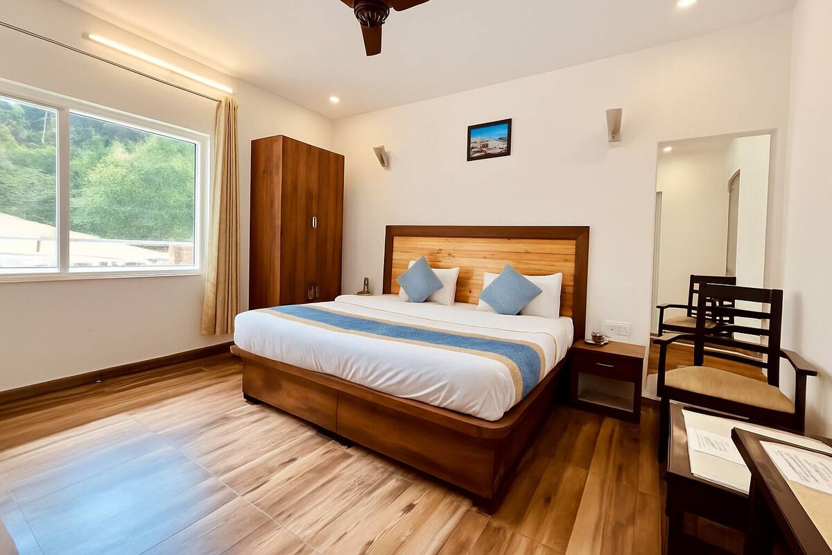 Habitación de hotel con una cama grande, armario de madera, escritorio con silla y ventana con cortinas.