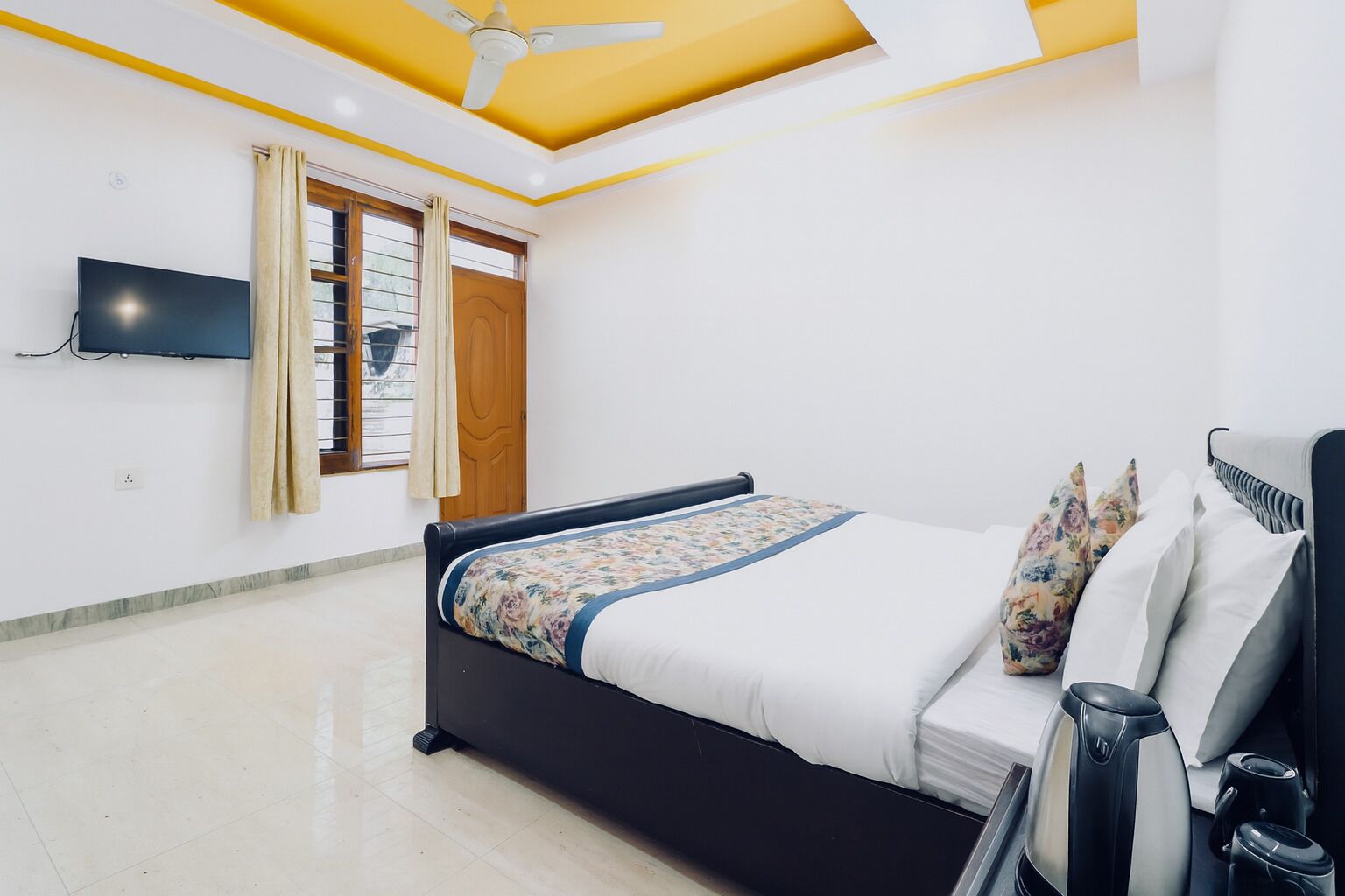 Une chambre à coucher avec un lit, un ventilateur de plafond, une télévision et une fenêtre avec des rideaux.