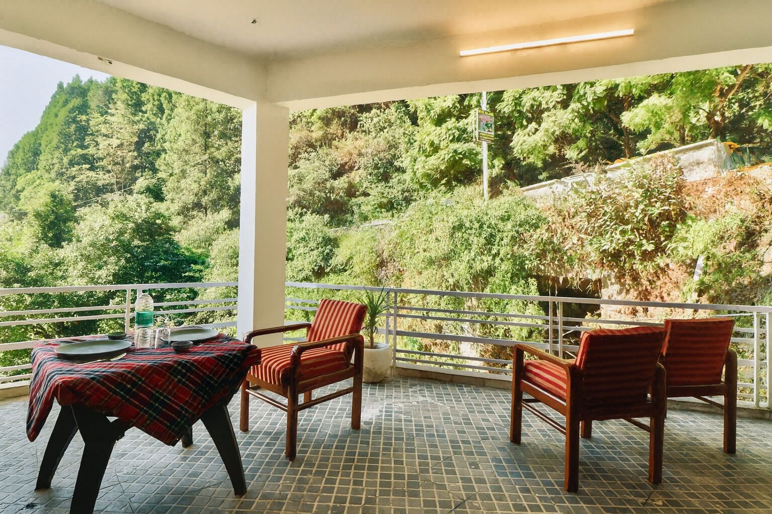 Un balcón con una mesa preparada para dos, sillas y vistas a una ladera boscosa.