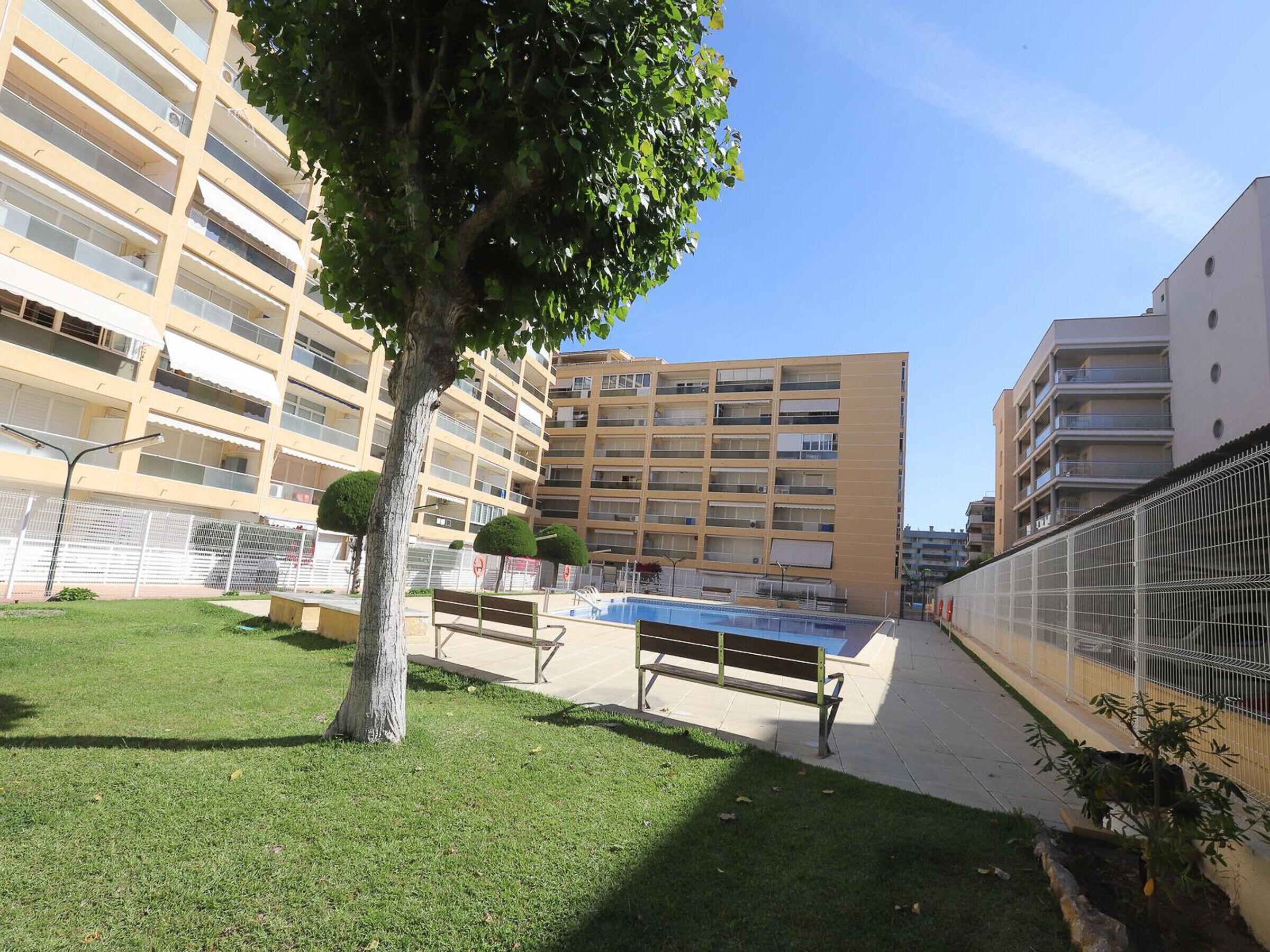 A residential building with multiple balconies, a swimming pool, and a fenced area with benches.
