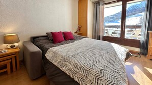 A bedroom with a bed, a nightstand, a lamp, a window with a view of a snowy landscape, and a wooden nightstand.