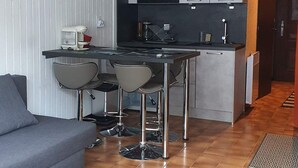 Une cuisine compacte avec un coin repas, comprenant un bar avec des tabourets et une machine à café.