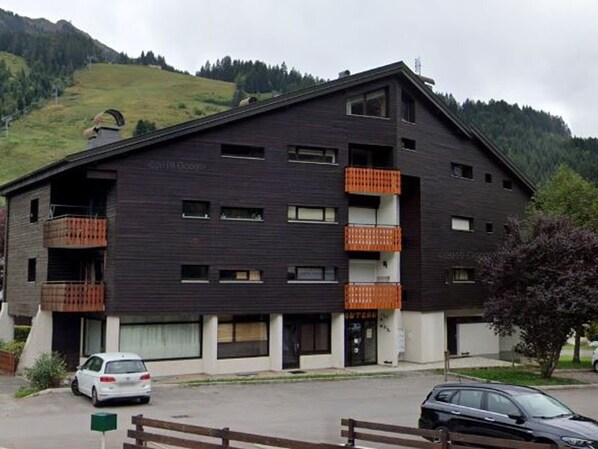 Un immeuble à plusieurs étages doté de balcons, d’un espace de stationnement et surplombant un paysage montagneux.