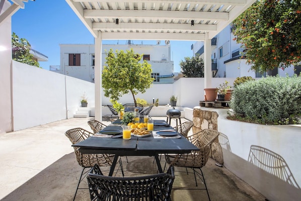 An outdoor patio with a table set for four, surrounded by wicker chairs, under a pergola.