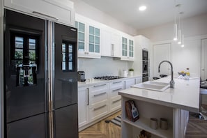 A modern kitchen with white cabinetry, stainless steel appliances, a built-in oven, and a large island with a sink.