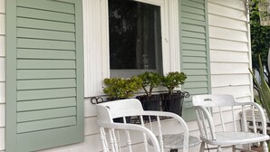 Une véranda avec deux chaises blanches, une fenêtre et des plantes en pot.
