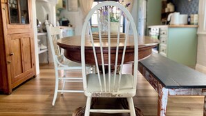 Un coin repas avec une table en bois et des chaises blanches, un banc et un meuble avec des portes en verre.