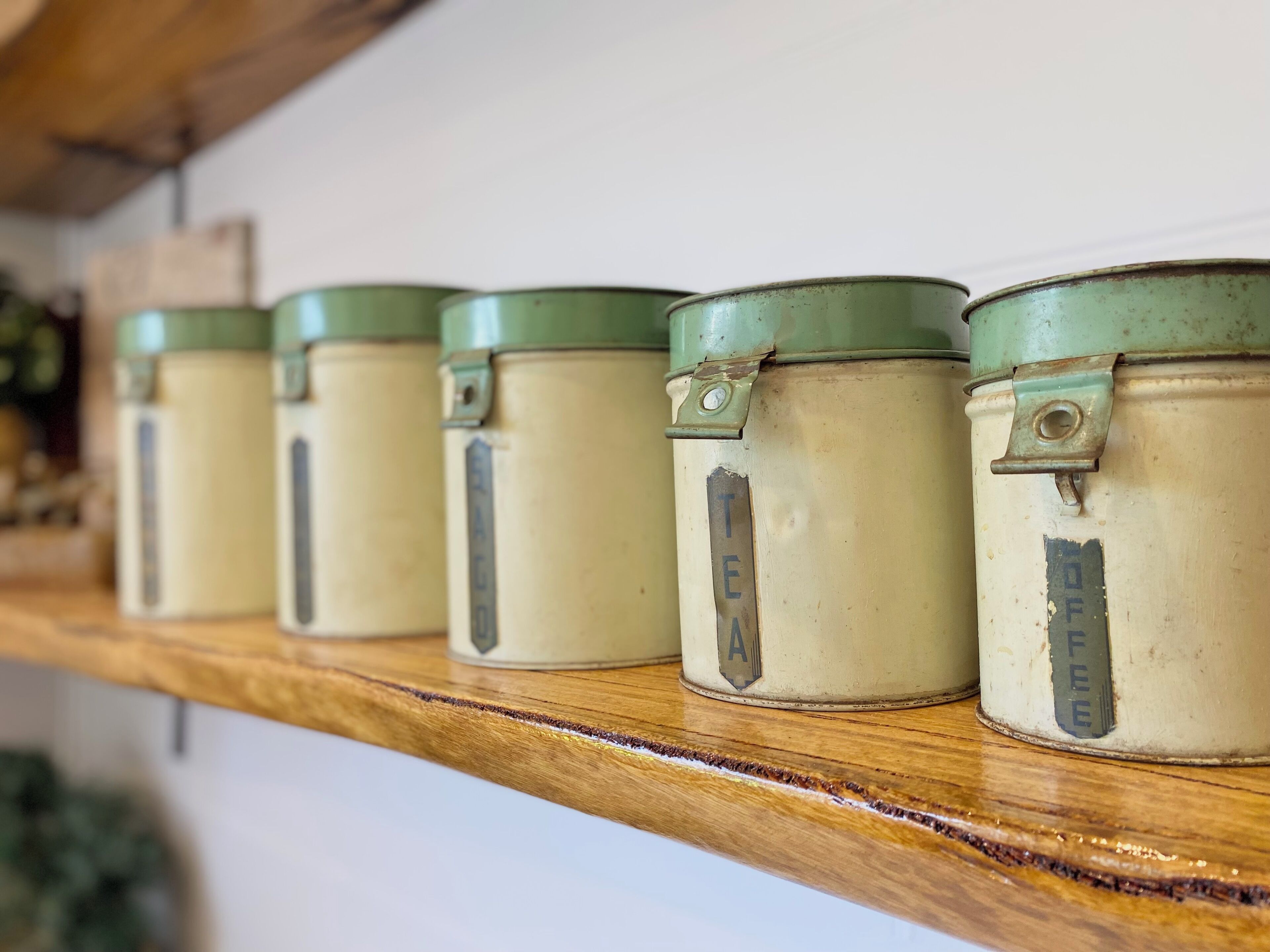 Une étagère en bois comportant cinq récipients en métal, chacun étant étiqueté avec le nom d’une boisson différente.